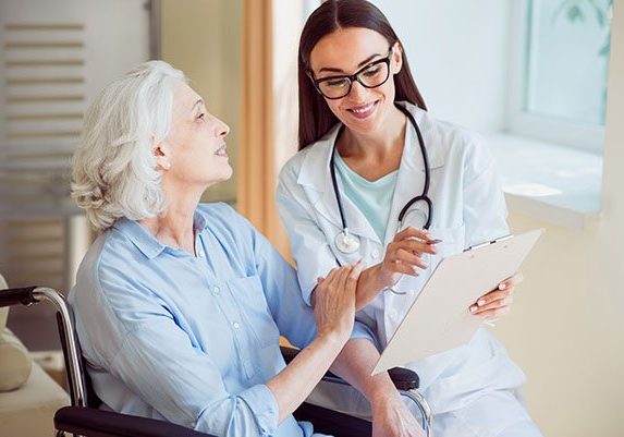 Nurse with her senior patient Trust. Happy senior woman and female merry and kind doctor holding clipboard and pen being at hospital ward
